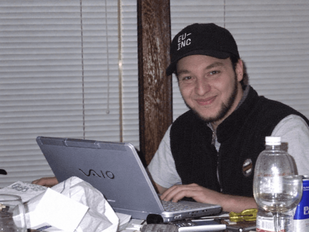 KI-modifiziertes Porträt von Georg mit schwarzer Kappe und Weste an einem Sony-VAIO-Laptop